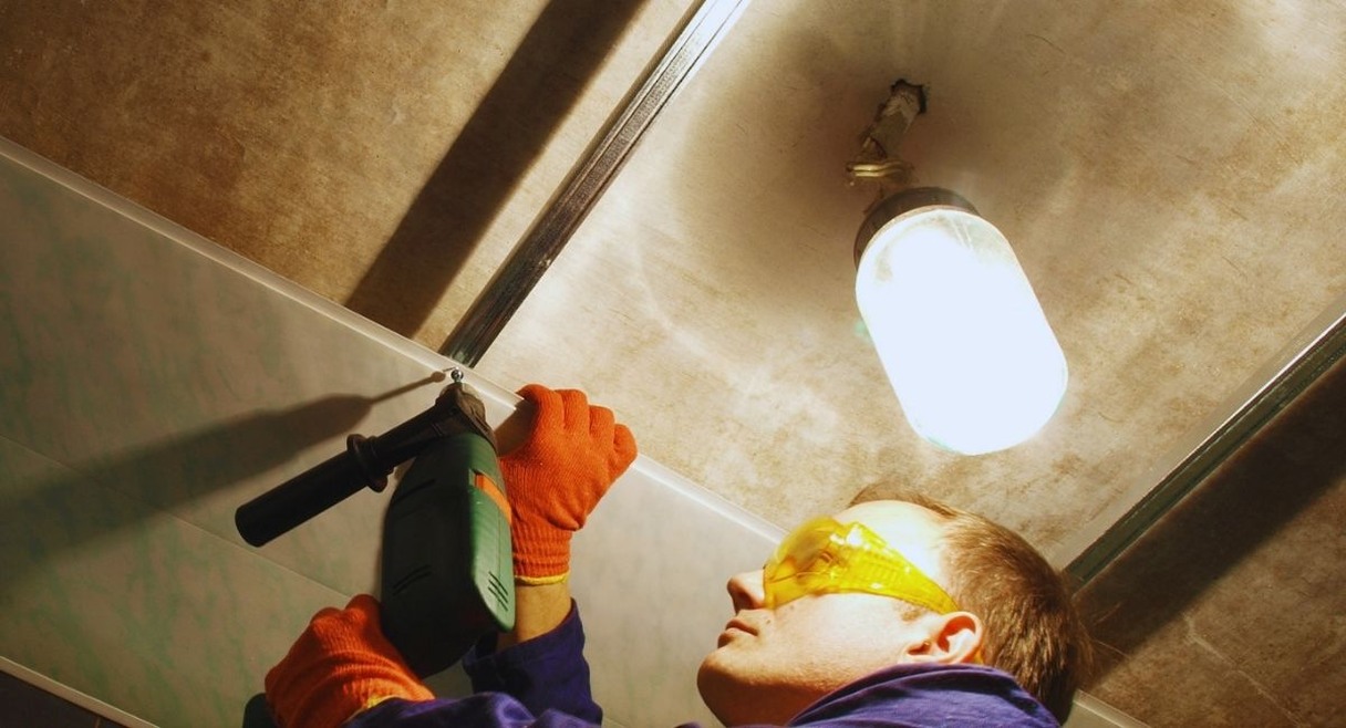 Ouvrier fixant un panneau de lambris PVC au plafond avec une perceuse